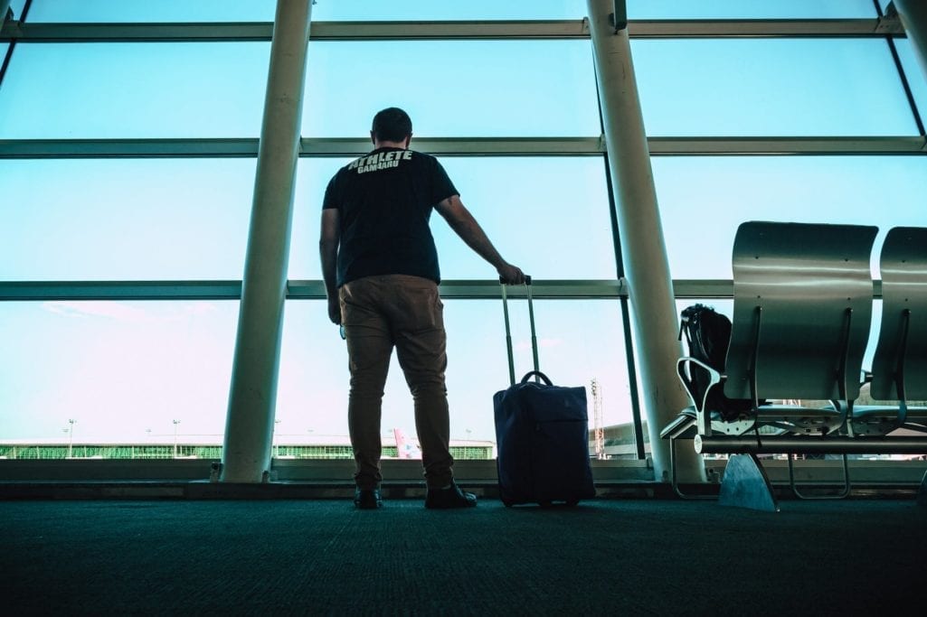 Man standing with suitcase looking out airport window