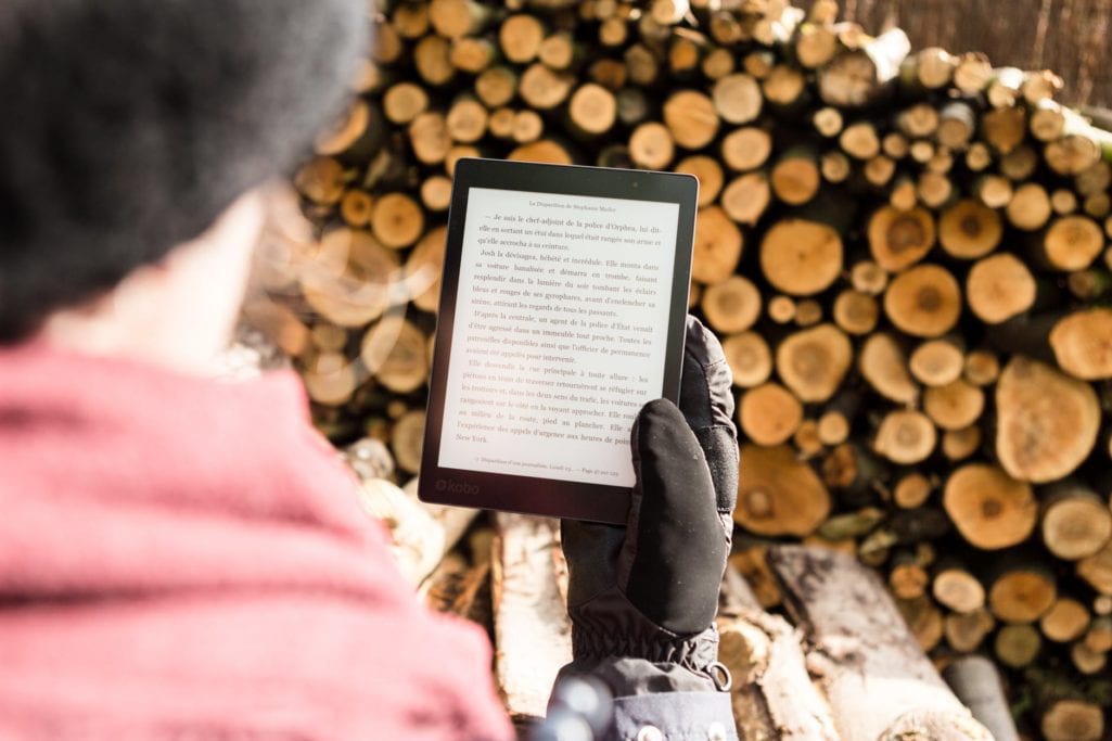 person holding black e book reader near pile of firewood