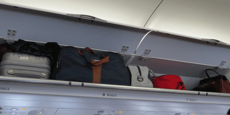 Image of bags stowed in overhead compartment on airplane - checked baggage vs carry on