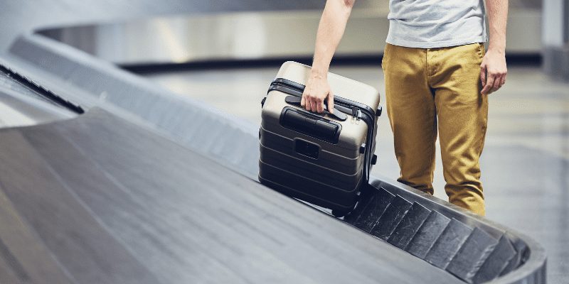 Image of man picking up a suitcase from baggage claim - checked baggage vs carry on