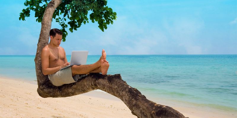 Image of man relaxing on palm tree with laptop